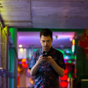 Hombre joven utilizando su teléfono móvil en un entorno urbano iluminado con luces de colores. Representa un enfoque reflexivo en la conexión digital, ideal para ilustrar el concepto de marketing consciente, donde la tecnología y la conciencia se encuentran para crear interacciones más auténticas y significativas.