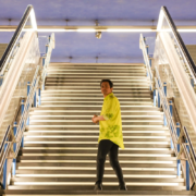Hombre con camisa amarilla de pie en unas escaleras iluminadas en una estación moderna, destacando el contraste entre la arquitectura y el individuo. Ideal para temas de comunicación y narrativa digital