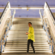 Hombre con camisa amarilla de pie en unas escaleras iluminadas en una estación moderna, destacando el contraste entre la arquitectura y el individuo. Ideal para temas de comunicación y narrativa digital
