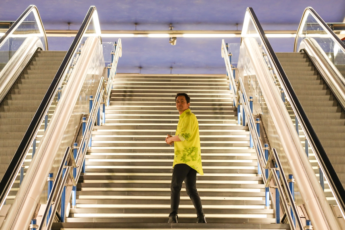 Hombre con camisa amarilla de pie en unas escaleras iluminadas en una estación moderna, destacando el contraste entre la arquitectura y el individuo. Ideal para temas de comunicación y narrativa digital