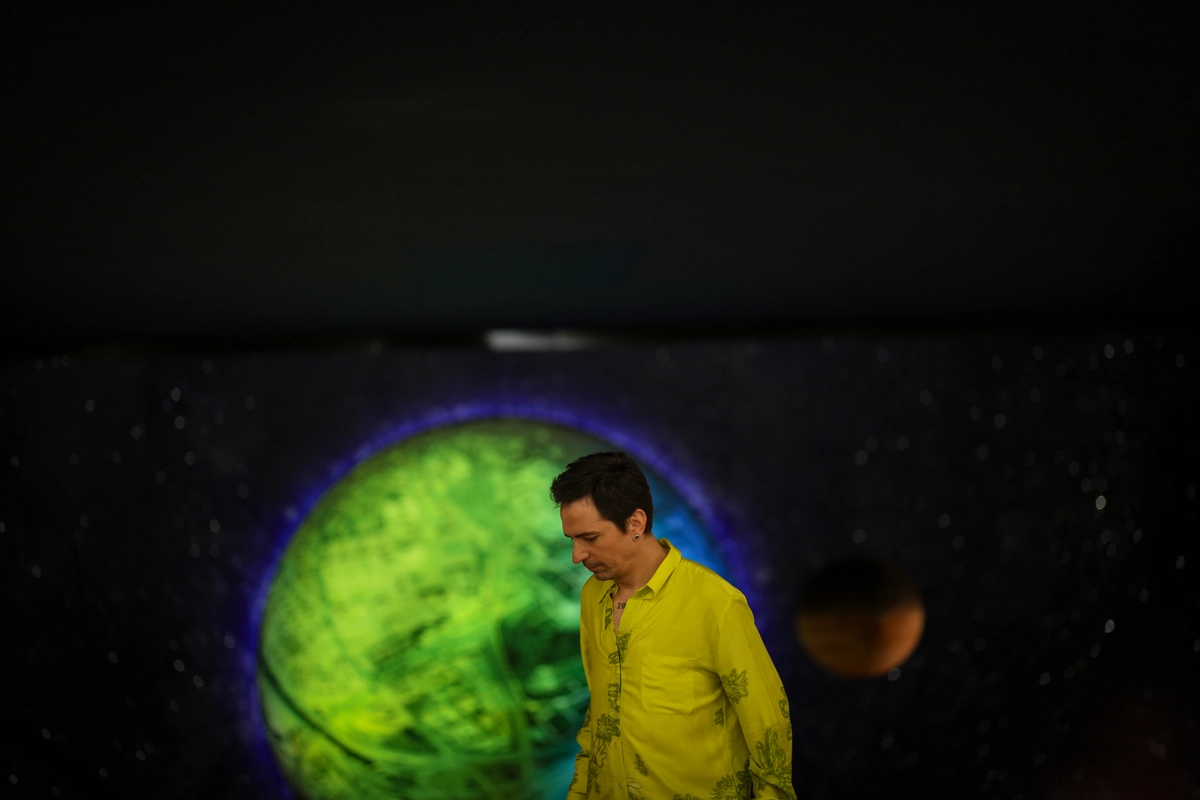Hombre con camisa amarilla de pie frente a un fondo de temática espacial con un planeta verde brillante. Esta imagen es ideal para representar temas de storytelling y comunicación visual creativa."