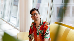 Ángel Román, consultor de comunicación, posando en un sofá amarillo con camisa colorida en un espacio moderno y luminoso
