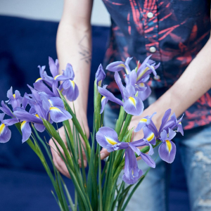 Persona colocando flores moradas en un jarrón, gesto simbólico de cuidado y respeto por la naturaleza como parte de una comunicación sostenible.